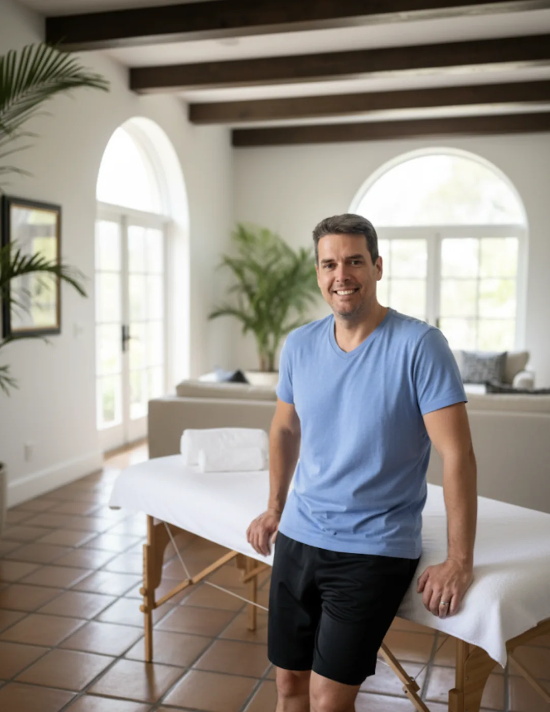 Photo shows James Palmer CMT leaning up against a massage table in the living room of a spanish style home in Beverly Hills, CA
